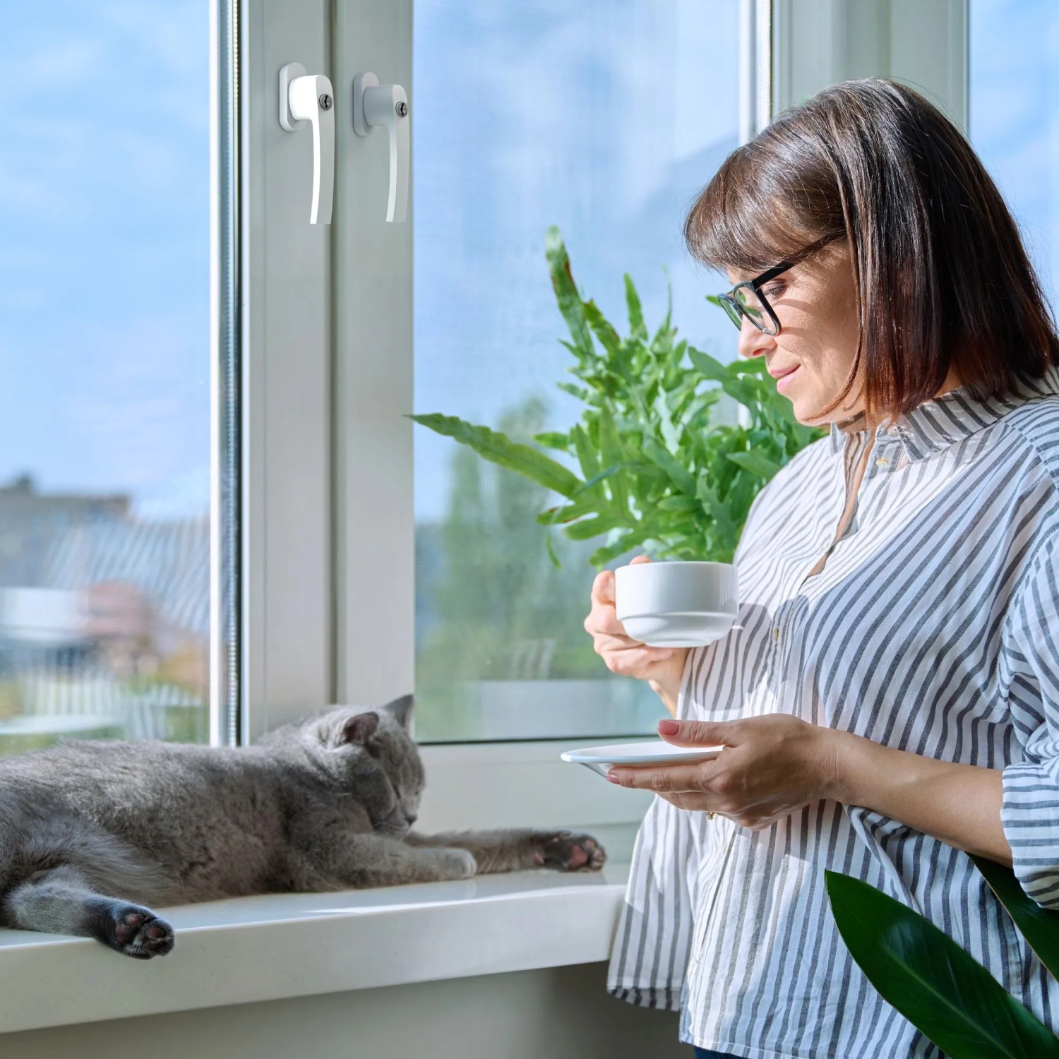 Frau mit Tasse am Fenster mit abschließbaren, weißen Basi Fenstergriffen und Katze.